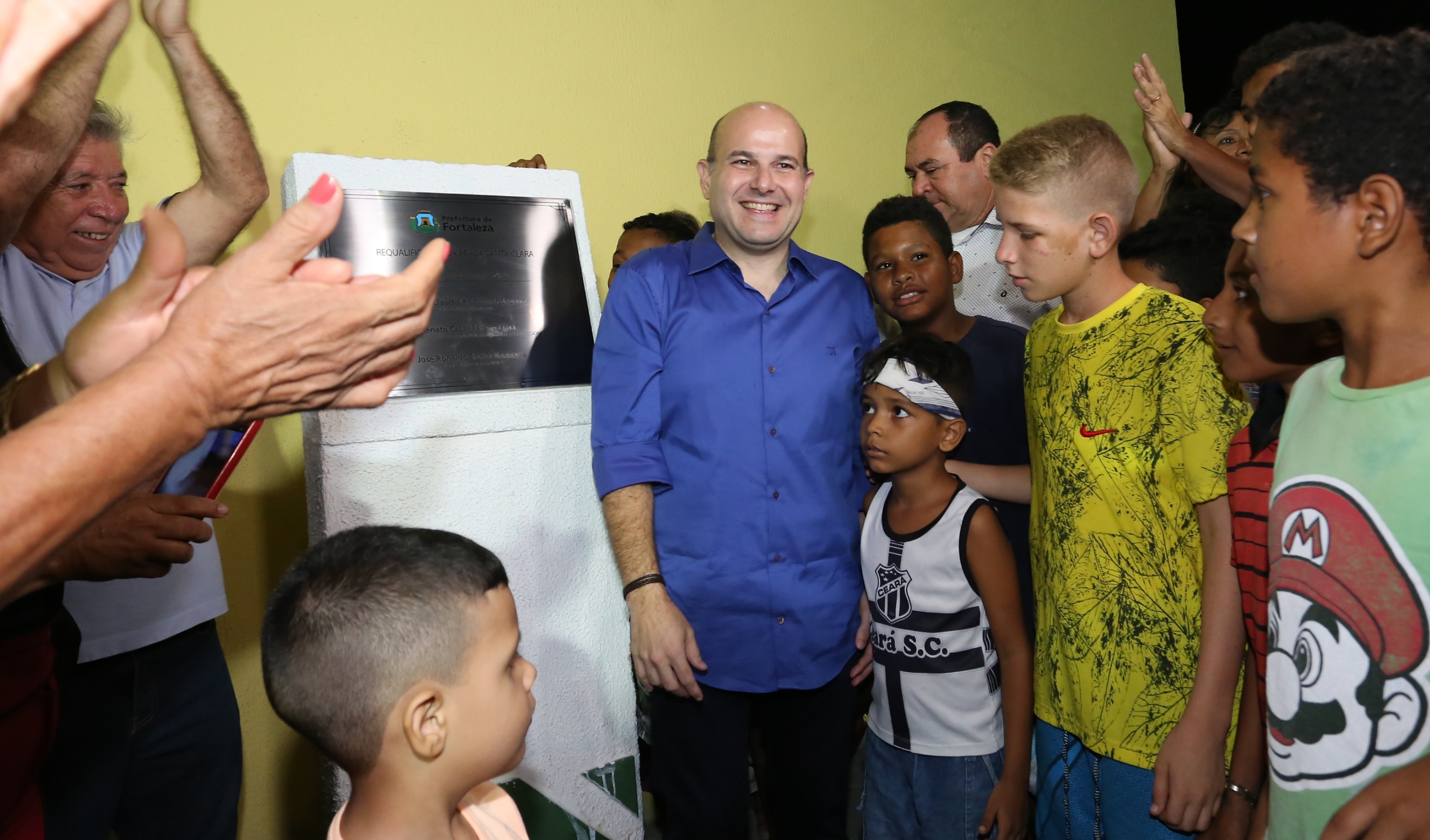 o prefeito está em frente à placa de inauguração, rodeado de crianças